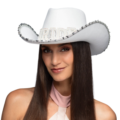 A smiling woman with long black straight hair has a white cowboy hat on with pail details and a band of shiny stones and the word 'Bride' on it in large letters.