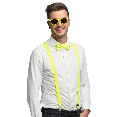 Lachende man draagt een witte blouse met donkere spijkerbroek in combinatie met een neon gele accessoireset bestaande uit een gele partybril, vlinderstrik en bretels.
