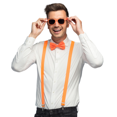 Lachende man draagt een witte blouse met donkere spijkerbroek in combinatie met een neon oranje accessoireset bestaande uit een oranje partybril, vlinderstrik en bretels.