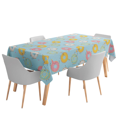 Een rechthoekige tafel met een lichtblauw tafelkleed erop dat versiert is met feestende donuts in 3 verschillende kleuren.