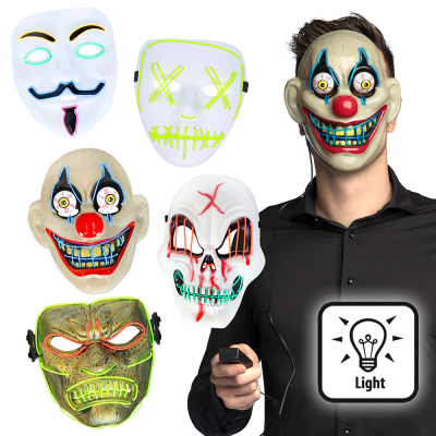 Man met Halloween LED masker van een horror clown op zijn hoofd en in zijn hand een zwarte afstandsbediening. Links daarvan zie je een masker van een een skull, een killer, een hacker, een horror clown en een samurai.