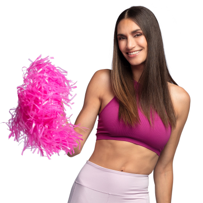 Lachende vrouw met lang steil bruin haar heeft een lichtroze sportbroek en roze sporttop aan en houdt een roze pompom vast.