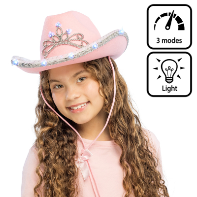 Une fillette souriante porte un chapeau de cow-boy rose pâle. Le chapeau de cow-boy est orné à l’avant d’un diadème de princesse qui s’illumine et, sur le bord, d’un ruban pailleté avec un éclairage LED intégré.