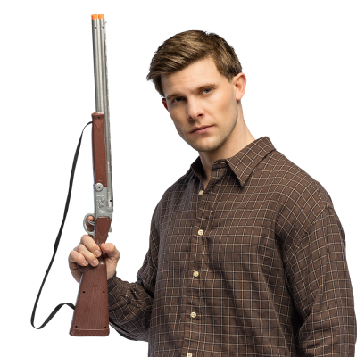 Un jeune homme porte une chemise western brun foncé et tient un faux pistolet classique avec des détails bruns et argentés pour accessoiriser son look de cow-boy dur.