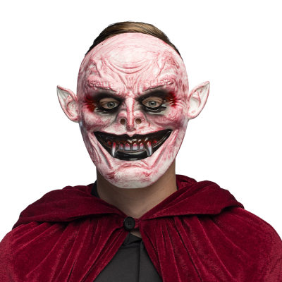 Un homme porte un costume d'Halloween avec une cape bordeaux et un masque monstrueux de vampire avec une peau rouge effrayante, des oreilles pointues et un large sourire avec des crocs acérés.