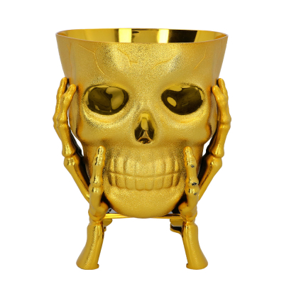Gouden schaal in de vorm van een schedel met skelet�handen � opvallende Halloween kom voor drankjes, snoep of decoratie.