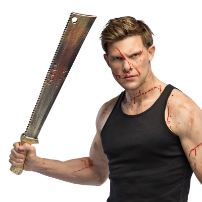 A man is covered in fake blood splatters and stands in a menacing pose holding in his hand a fake machete with gory details to complete his Halloween look.