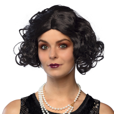 Een lachende vrouw is gekleed in jaren 50 flapper stijl en heeft een pruik op met korte zwarte krullen.