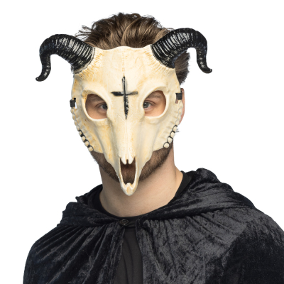 Ein Mann trägt einen langen, schwarzen Umhang und im Gesicht die Maske eines dämonischen Widderskeletts mit großen schwarzen Hörnern und einem Kreuz auf der Stirn.
