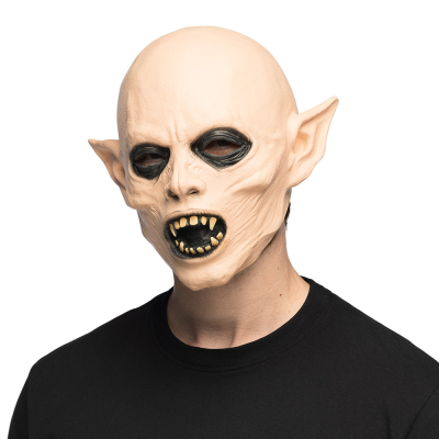 A man wearing a black t-shirt has on his head a Halloween latex mask of a vampire monster with dark eyes, long pointed ears and sharp teeth.